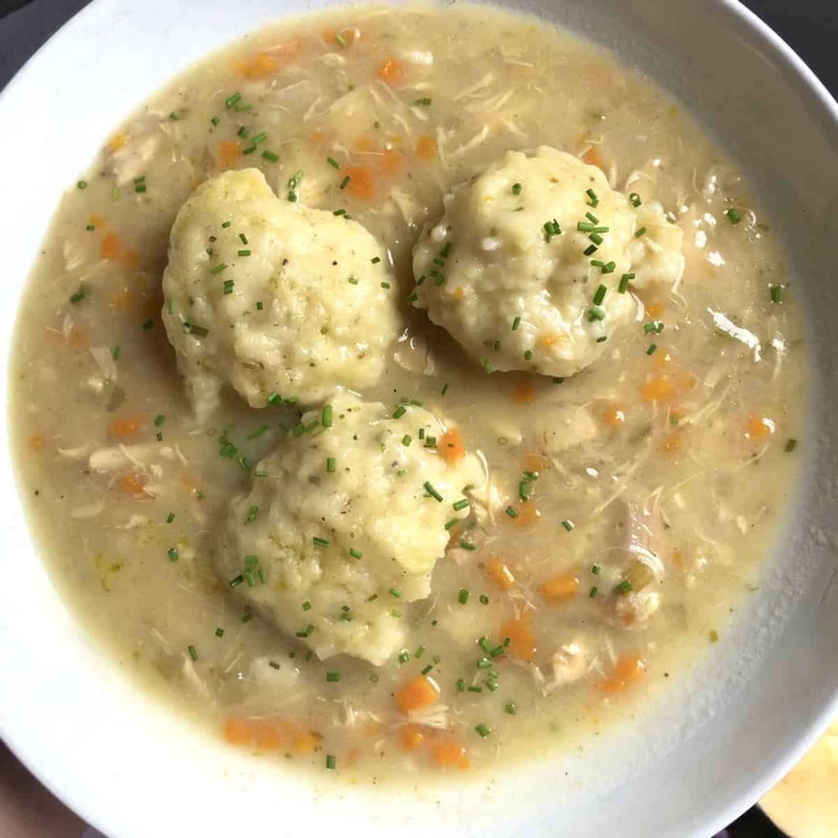 A shallow bowl of chicken and dumpling soup with three drop dumplings in the center ready to eat.