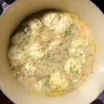A Le Creuset pot of finished chicken and dumplings soup with fluffy drop dumplings and chopped parsley.