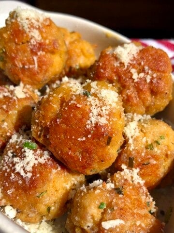 Golden brown chicken and pork meatballs in a ceramic dish sprinkled with grated parmesan cheese and chives.