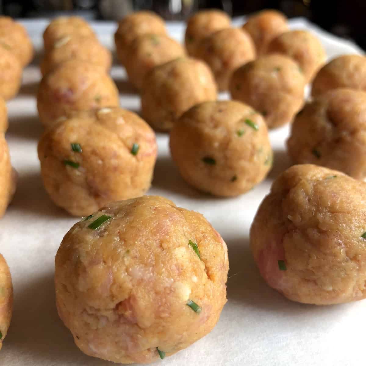 Raw chicken and pork meatballs rolled and arranged on a parchment lined baking sheet ready to bake for an easy meatball recipe.