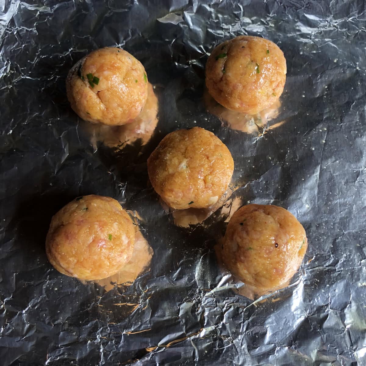 Raw chicken meatballs on an aluminum foil-lined sheet pan ready to be baked.