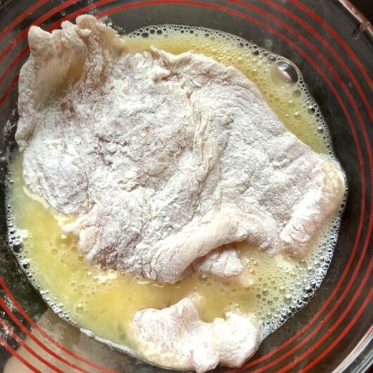 turkey breast cutlet completely immersed in beaten egg wash