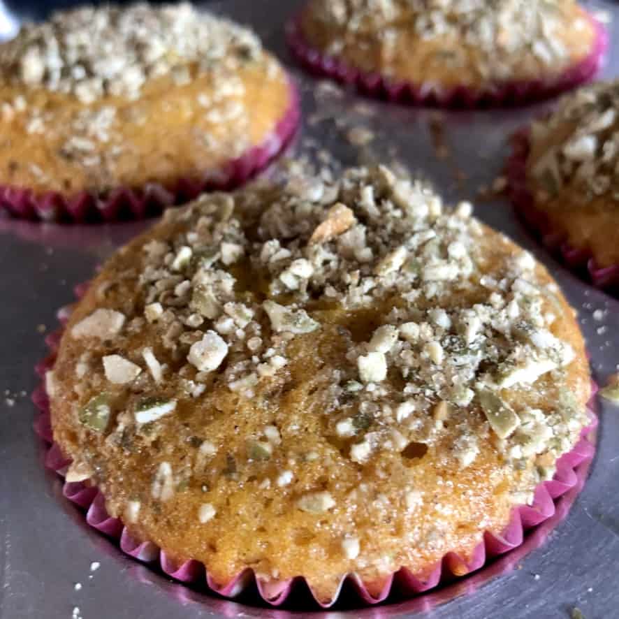 closeup pumpkin spice muffin with toasted chopped pumpkin seeds on top in a muffin tray