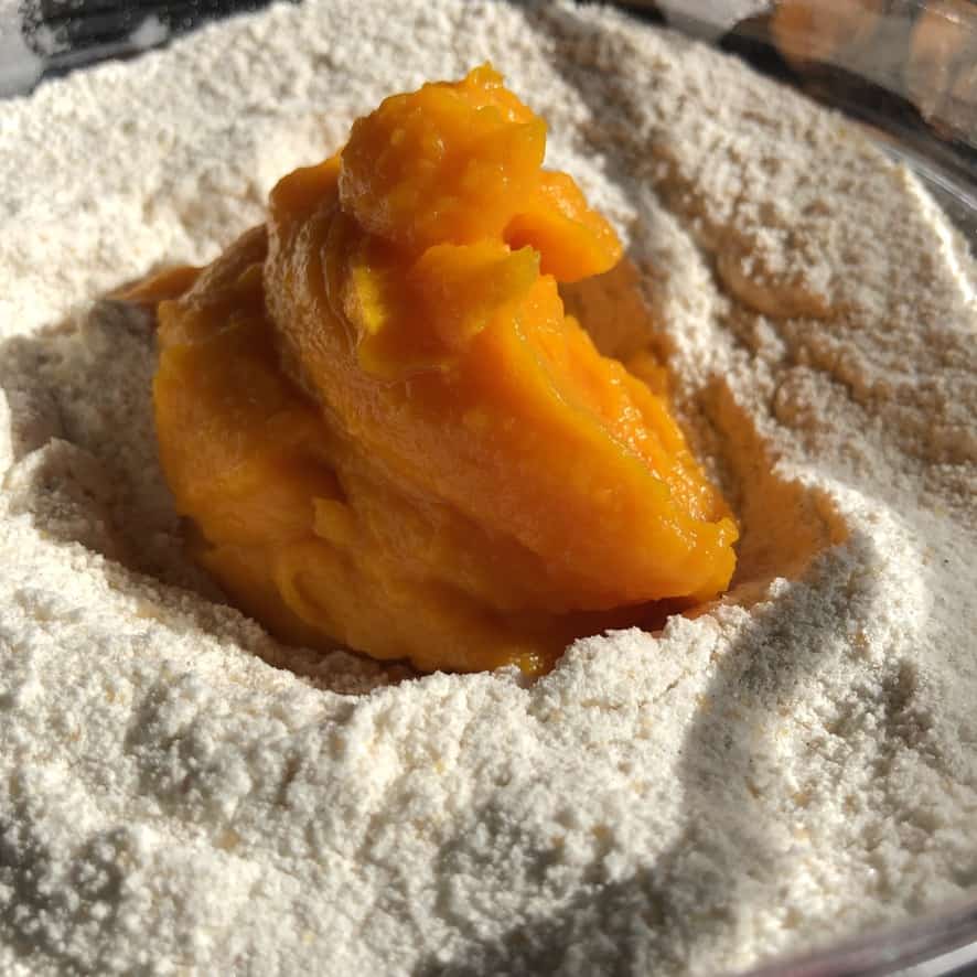 a scoop of bright orange pumpkin purée in the middle of a bowl with flour and other dry ingredients