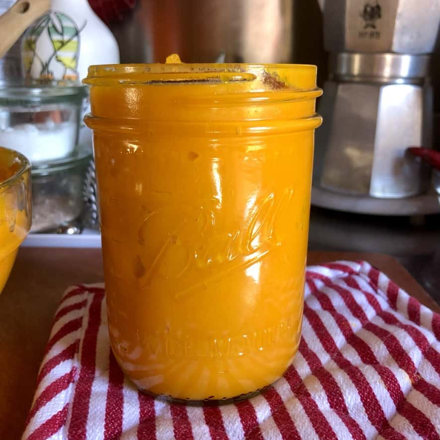 a Ball Mason widemouth pint jar filled to the top with homemade bright orange pumpkin purée resting on a red and white striped pot holder