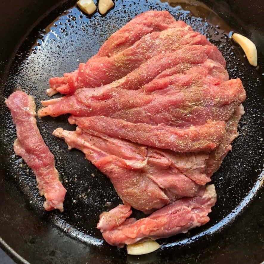 seasoned butterflied turkey leg searing in a cast iron skillet with blistered garlic cloves