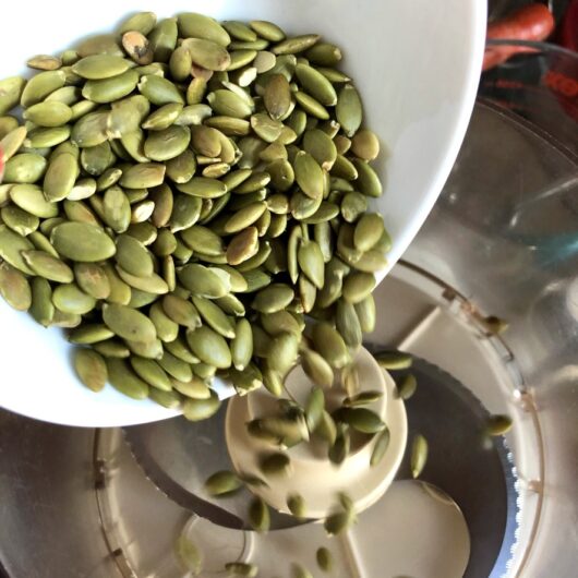 toasted pumpkin seeds being added to a food processor