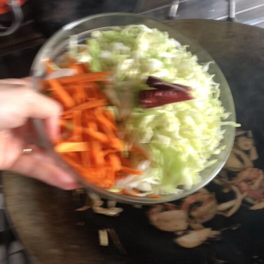 julienned carrots, shredded cabbage. and chili peppers in a prep bowl being added to the wok