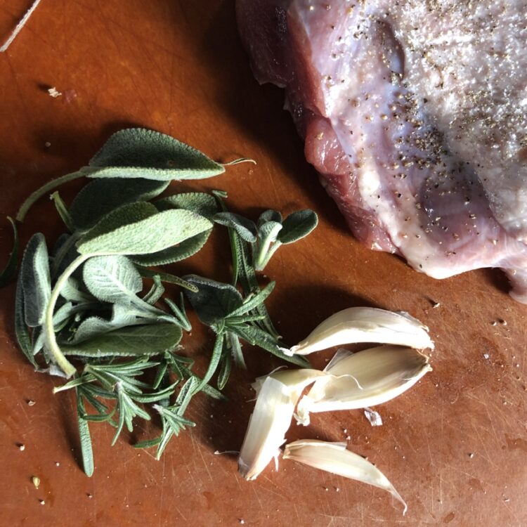 fresh sage and rosemary leaves next to garlic cloves on a cutting board