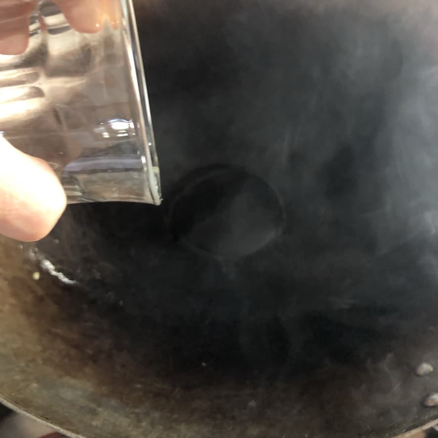 pouring the last half of the oil into the wok