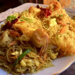 closeup of singapore noodles on an oval platter with the sunlight hitting it