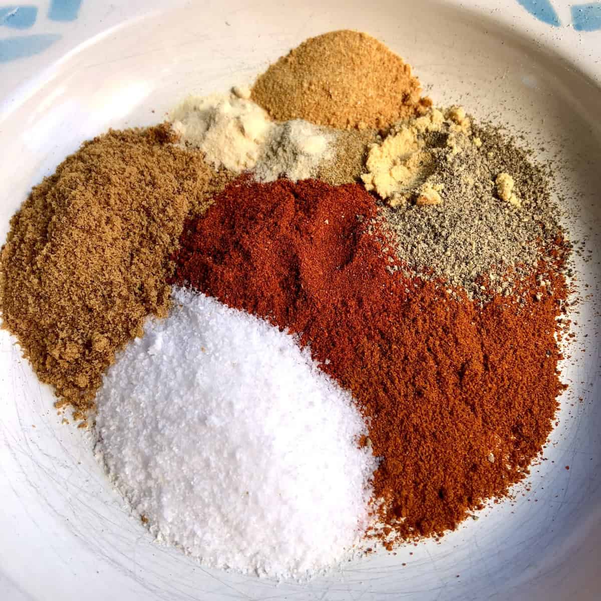 Dried spices in mounds in a shallow bowl showing all the best spices to use for making homemade BBQ seasoning blend (aka BBQ dry rub).
