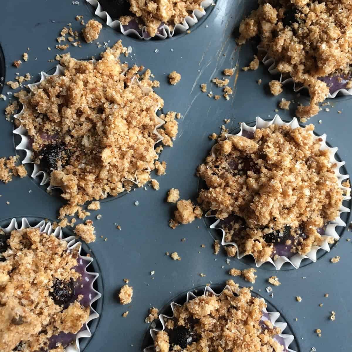A muffin tin of blueberry muffins topped with streusel crumb topping ready to bake.
