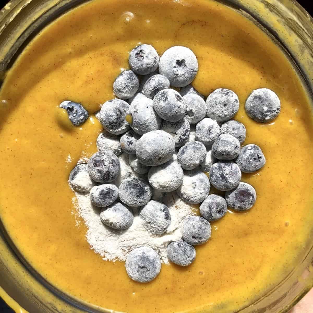 Pumpkin muffin batter in a bowl with floured blueberries added and ready to fold in.
