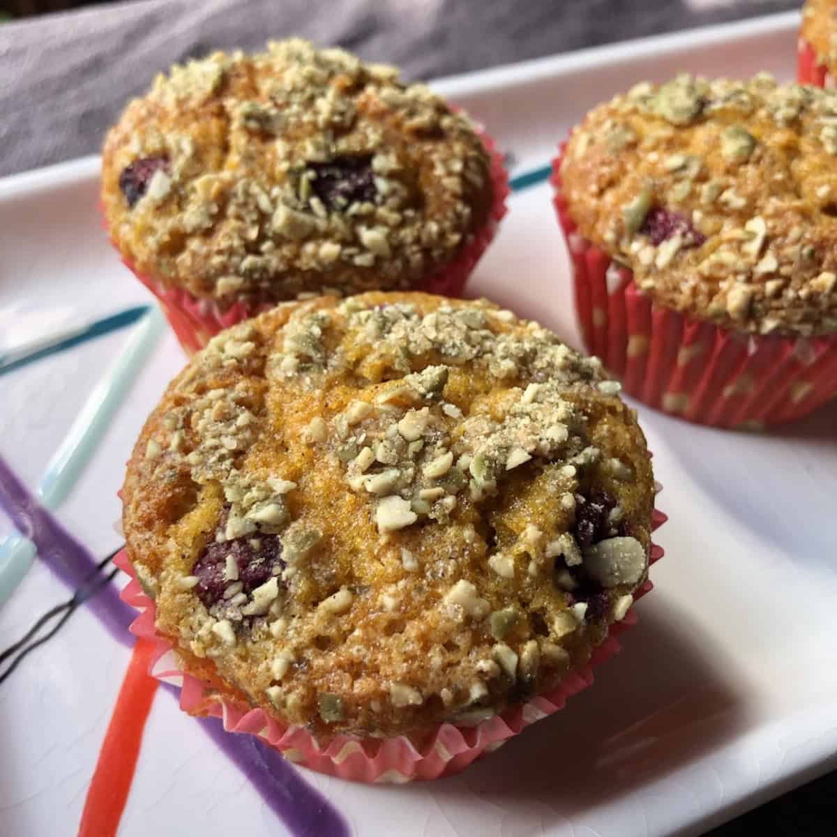Three raspberry pumpkin muffins on a tray with whole raspberries visible in the tops.
