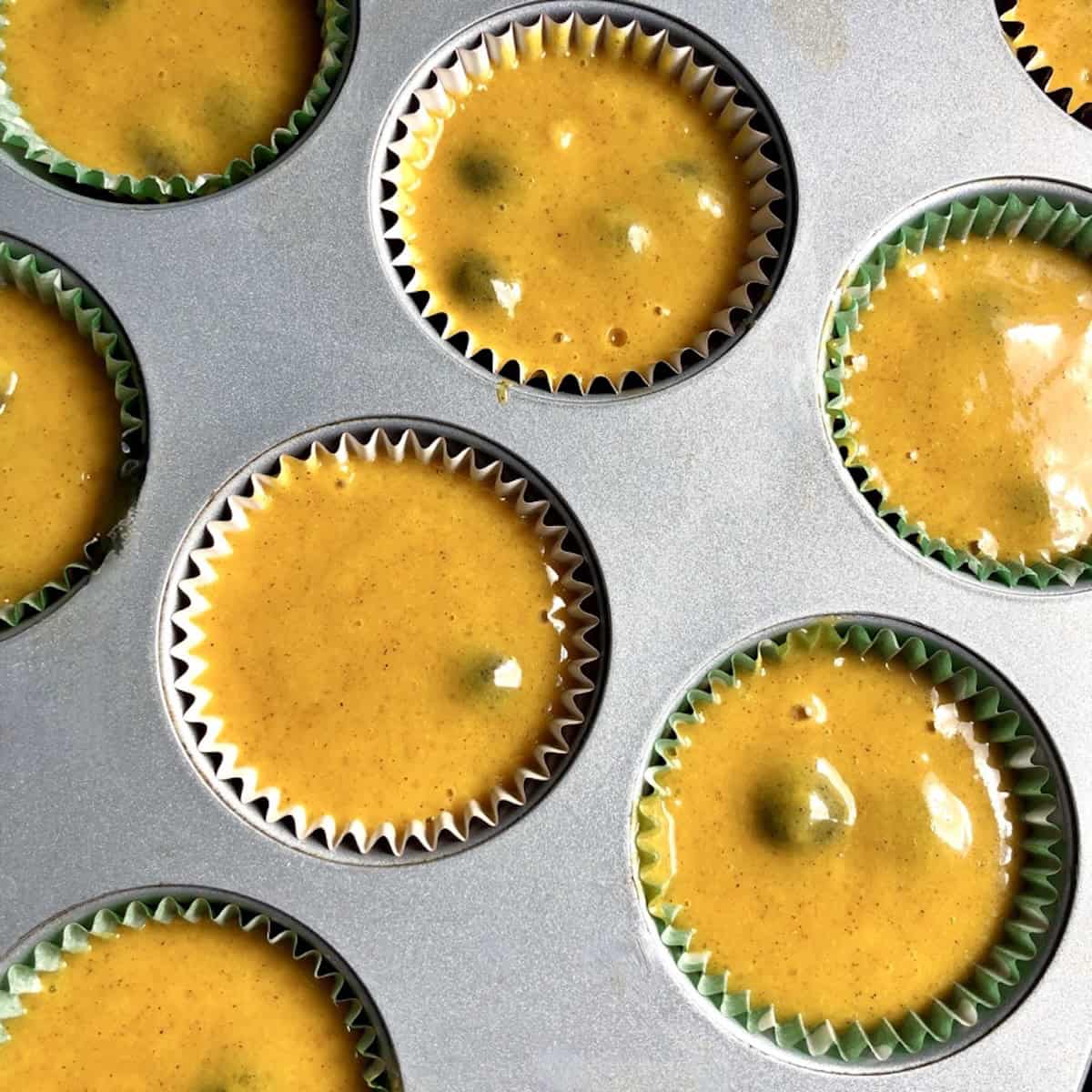 A muffin tin filled with blueberry pumpkin muffin batter in paper liners ready to bake.
