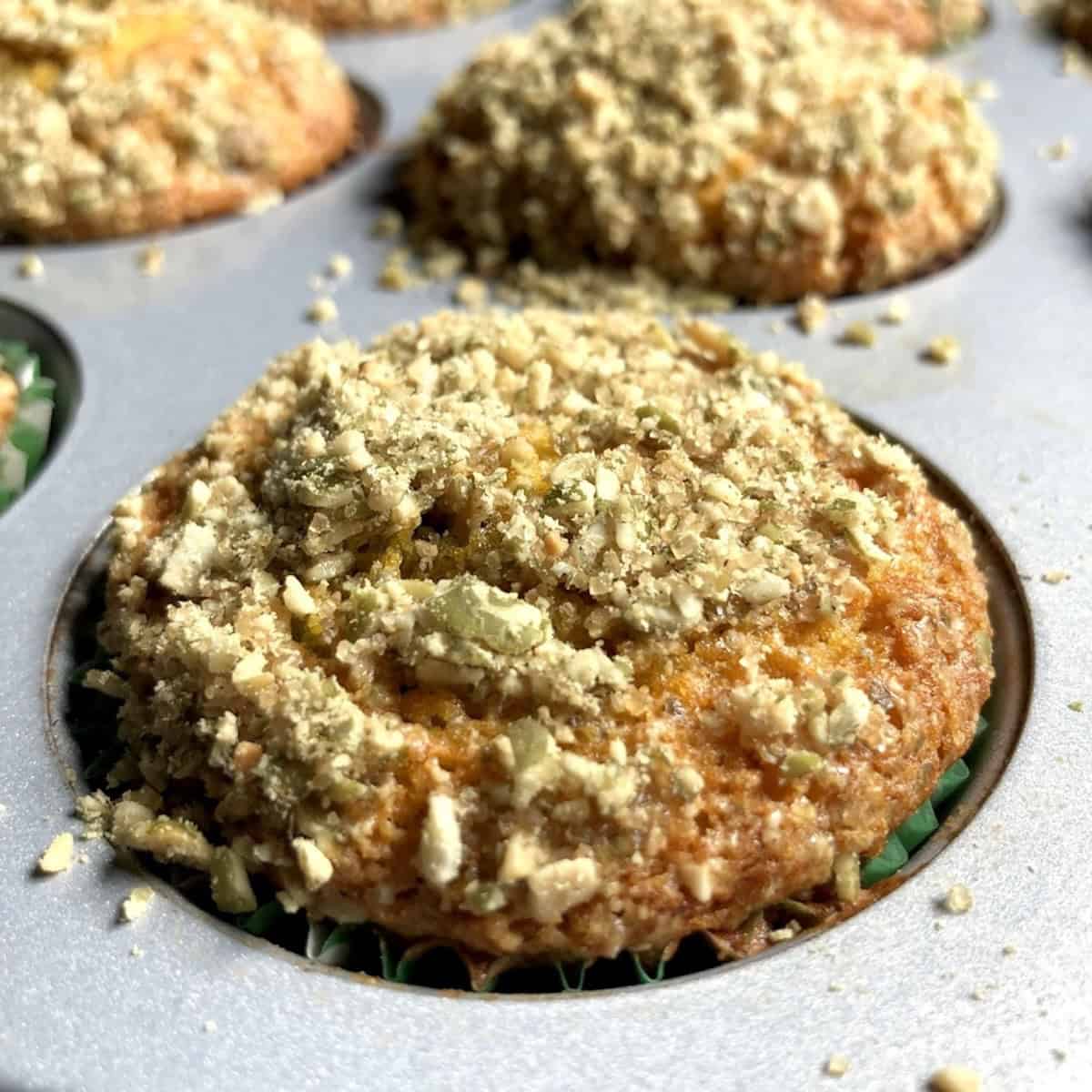 Fully baked pumpkin muffins with golden tops and pumpkin seed crunch topping in the muffin tin.