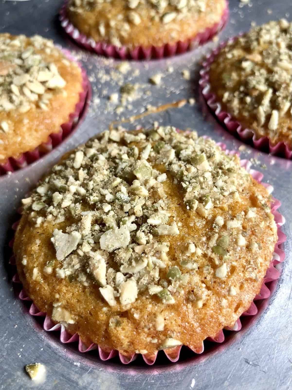 Tall domed pumpkin streusel muffins with pumpkin seed crunch topping in a muffin tin showing the high bakery style rise.
