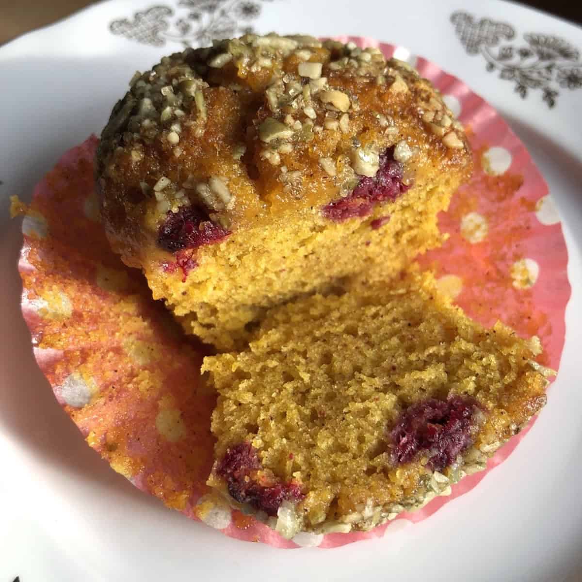 A raspberry pumpkin muffin sliced open revealing whole raspberries baked inside the pumpkin spice crumb.
