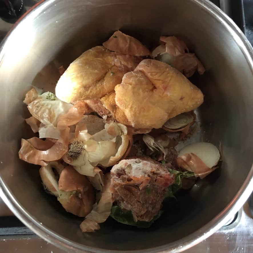 A pressure cooker with two chicken wings and leftover vegetable scraps that have. been saved in the freezer to make homemade chicken stock.