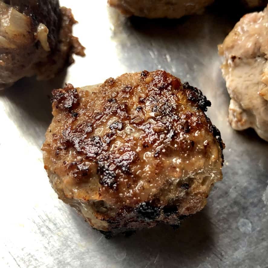 a closeup of a single meatball on a sheet tray after being cooked to perfectly golden brown