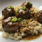 swedish meatballs in pan sauce on top of white rice and sprinkled with sliced green onions for garnish
