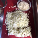 freshly grated mozzarella cheese along with some larger torn pieces and the grated Grana Padano cheese in a bowl next to it