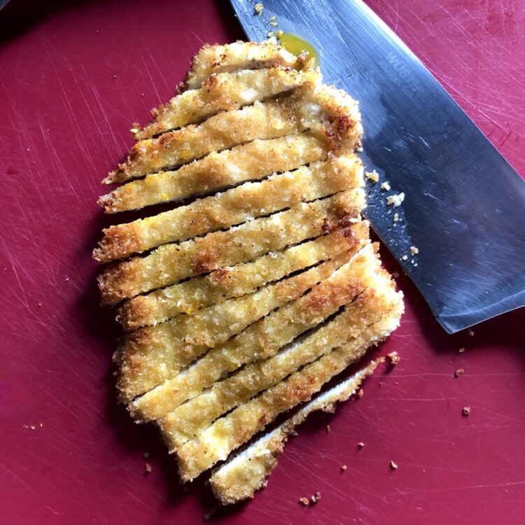 sliced breaded chicken cutlet on a cutting board