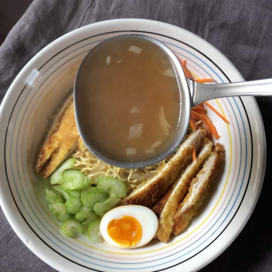 adding boiling chicken soup base broth to the bowl of ramen like soup