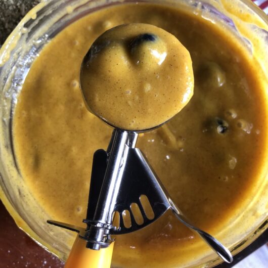 a measuring scoop with pumpkin spice blueberry batter in it