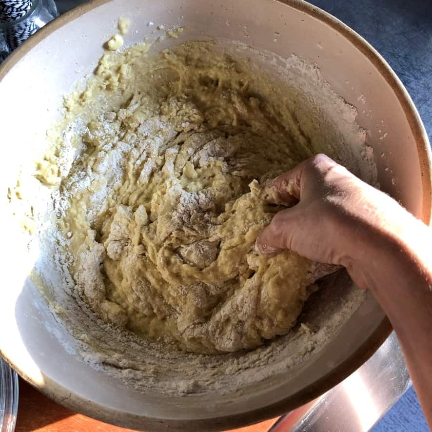 Adding flour and mixing the homemade cinnamon roll dough in a bread bowl.