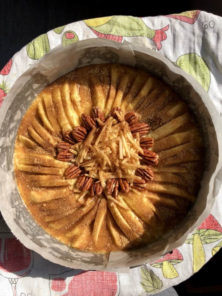 unbaked apple cake with spices and sugar mixture covering the entire top and a ring of pecans around the middle