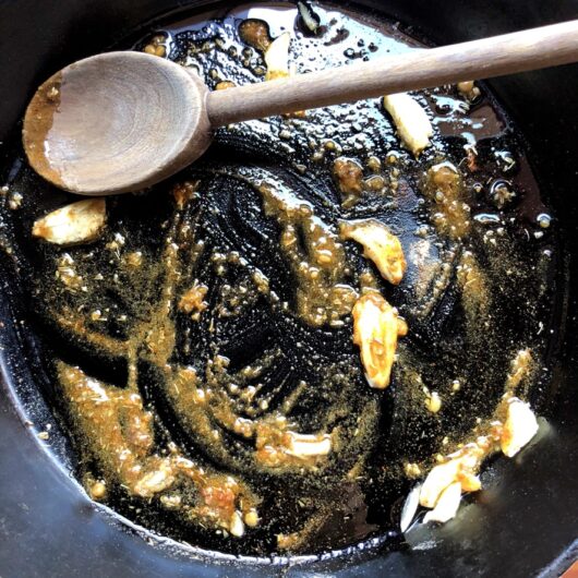 toasting spices with garlic and oil in a cast iron skillet