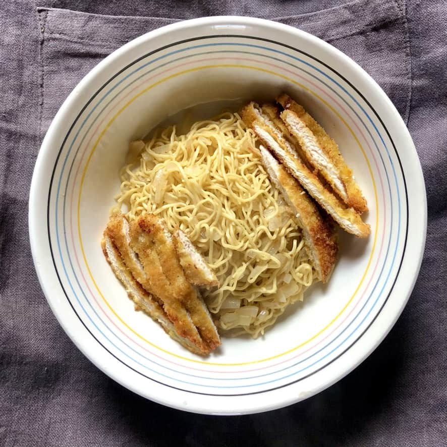 a ramen bowl with a pile of just cooked egg noodles (that look like ramen noodles) in the center with sliced chicken cutlets on opposite sides of the bowl