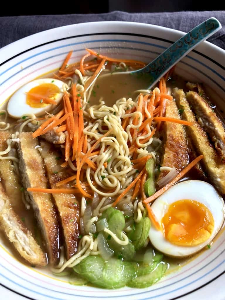 homemade chicken noodle oup with homemade noodles, sliced breaded chicken cutlet , two halves of ramen eggs with soft jammy yolks, julenned carrots, paper-thin slices of celery, and homemade swimming in homemade chicken stock with a ramen spoon