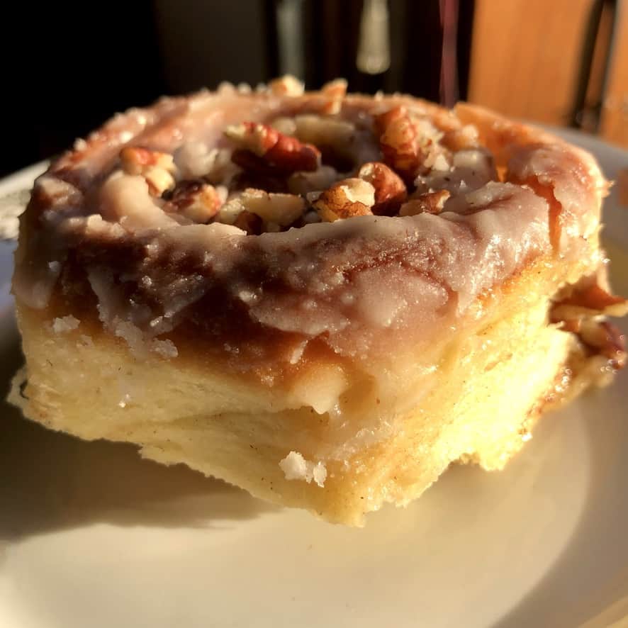 a large visibly fluffy cinnamon roll with pecans on top