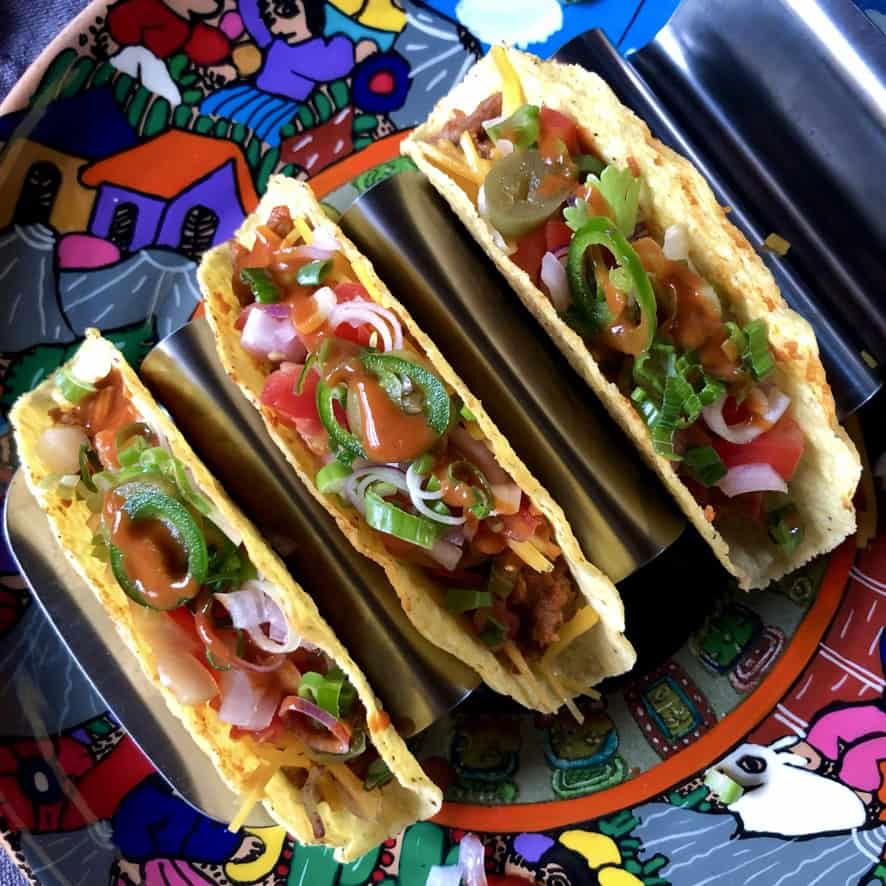 3 turkey tinga tacos in hard tortilla shells with hot sauce drizzled on top