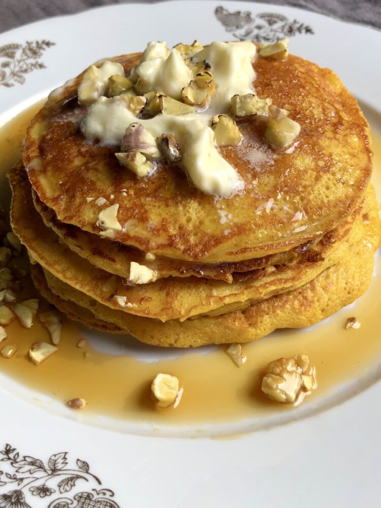 a serving platter with a stack of beautiful pumpkin-colored pancakes with melting butter, toasted chestnuts and covered with maple syrup