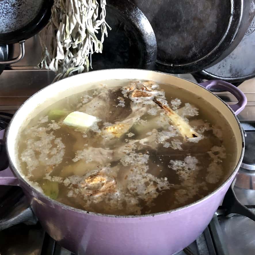 tonkotsu broth boiling away in a dutch oven with the skum having been partially skimmed off