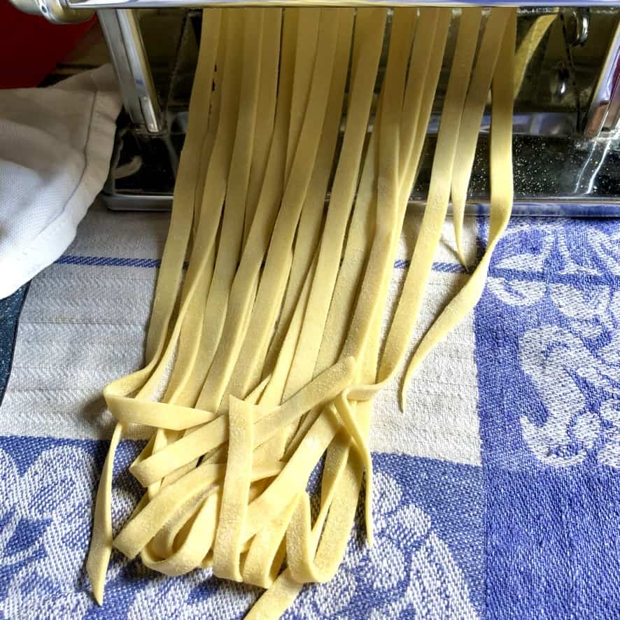 long ribbon-like noodles coming out of the pasta machine being cut by the fettuccine attachment