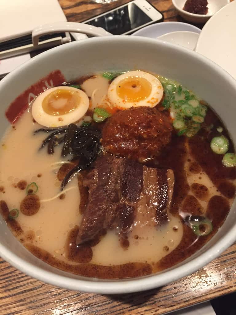 A bowl of ramen with custardy ramen eggs floating in the broth with tender chashu pork and a large mound of spicy tare topping