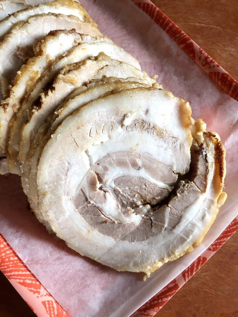 rolled, braised pork chashu sliced and ready to heat and eat layered on a coral colored platter with Japanese fan motif design