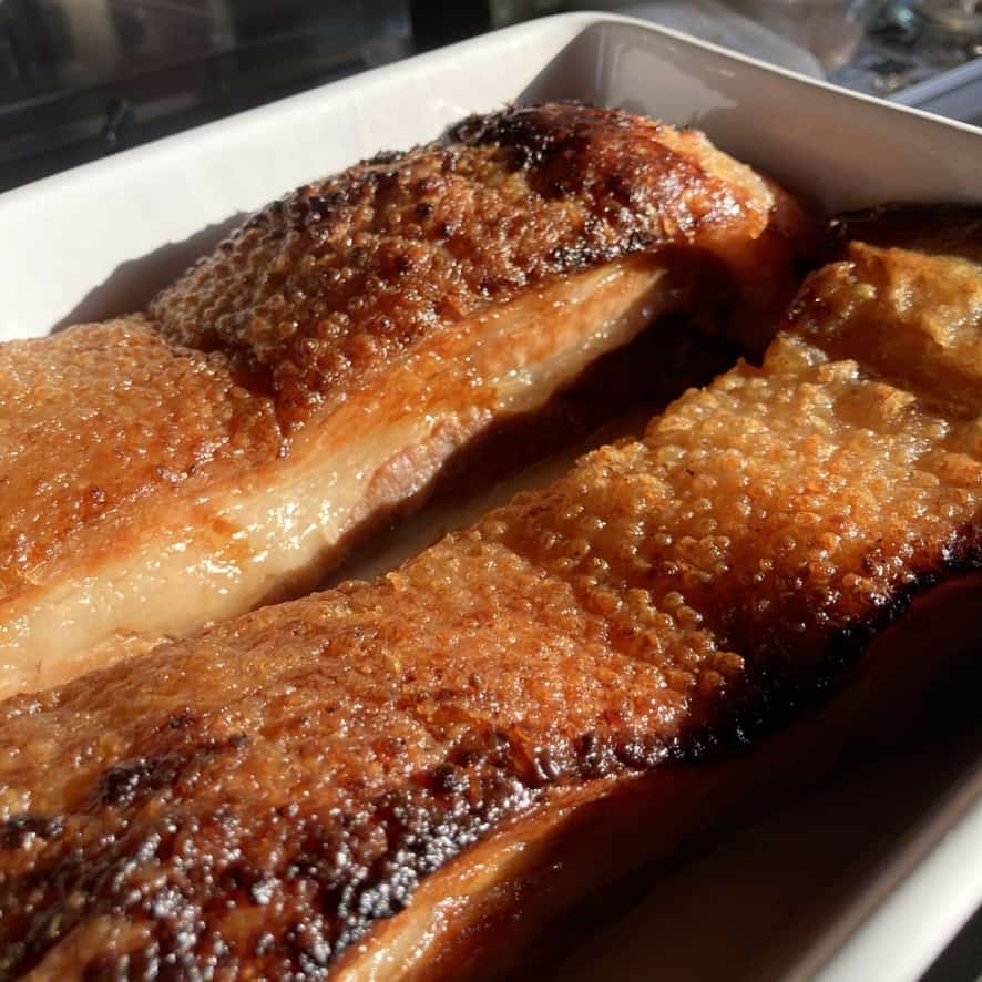 two long pieces of golden brown braised pork belly in a white ceramic casserole dish