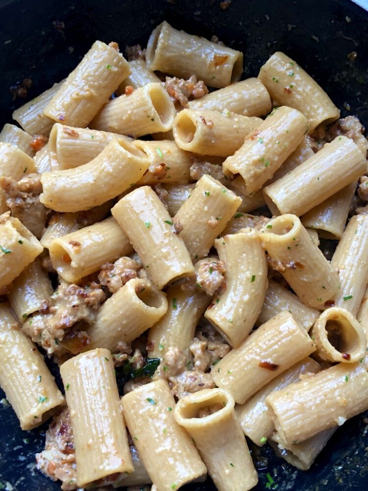 a sauté pan full of just tossed creamy sausage and wine sauce with rigatoni