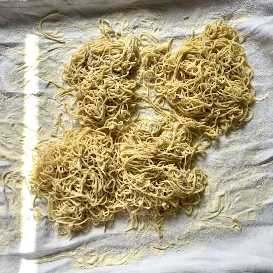 ramen looking egg noodles on a cloth covered with semolina flour after being dried and arranged in 4 nests