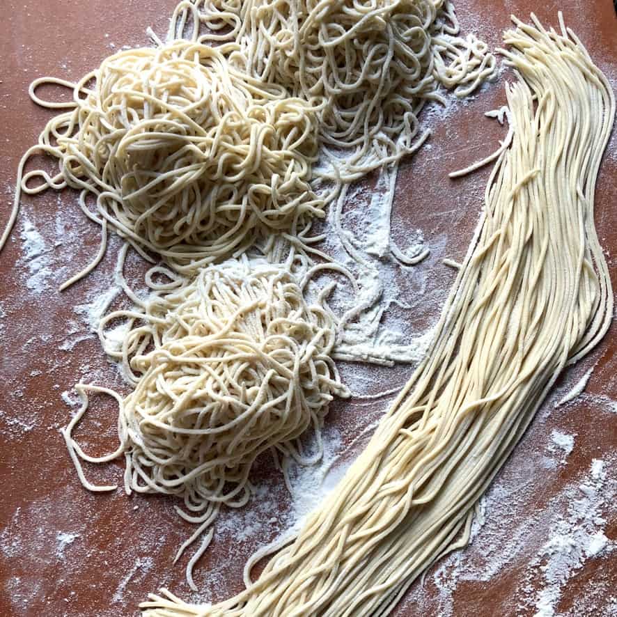 raw homemade ramen noodles on a cutting board that have been dusted with flour and nested with one group left long and lean so they aren't curly