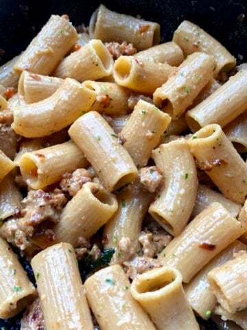 a sauté pan full of just tossed creamy sausage and wine sauce with rigatoni