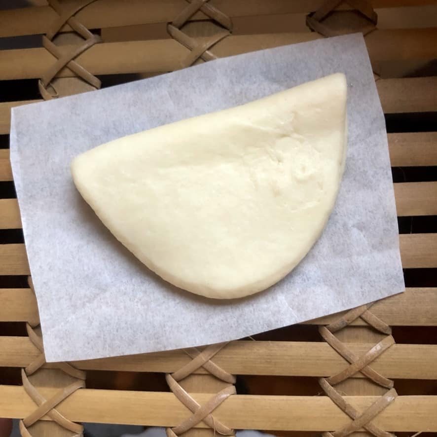 bun on a square of parchment paper in a steamer basket before being steamed