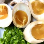 perfectly jammy caramel-coated ramen eggs on a tray with sliced scallions and fresh shitake mushrroms