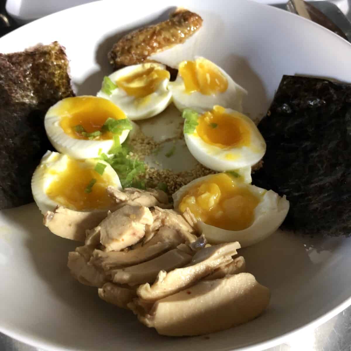 ramen toppings nested in a bowl around a pile of bouncy homemade ramen noodles